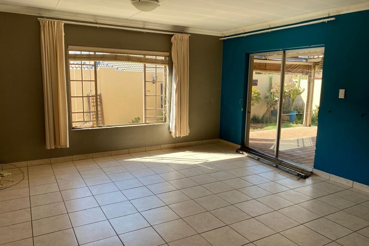 Spacious, empty living room featuring tiled flooring, large windows, and a sliding glass door providing direct access to the outdoor patio area.