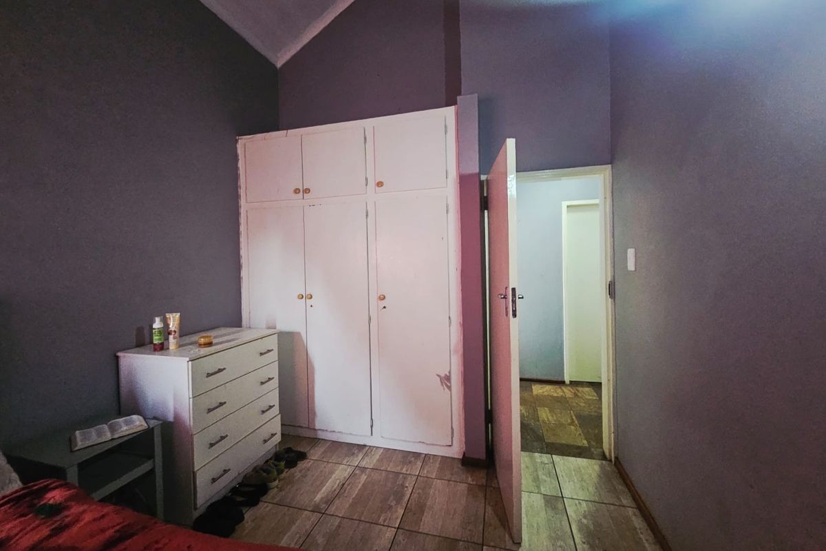 A bedroom featuring tiled flooring, a vaulted ceiling, and built-in cupboards, with an open doorway leading to an adjacent hallway.
