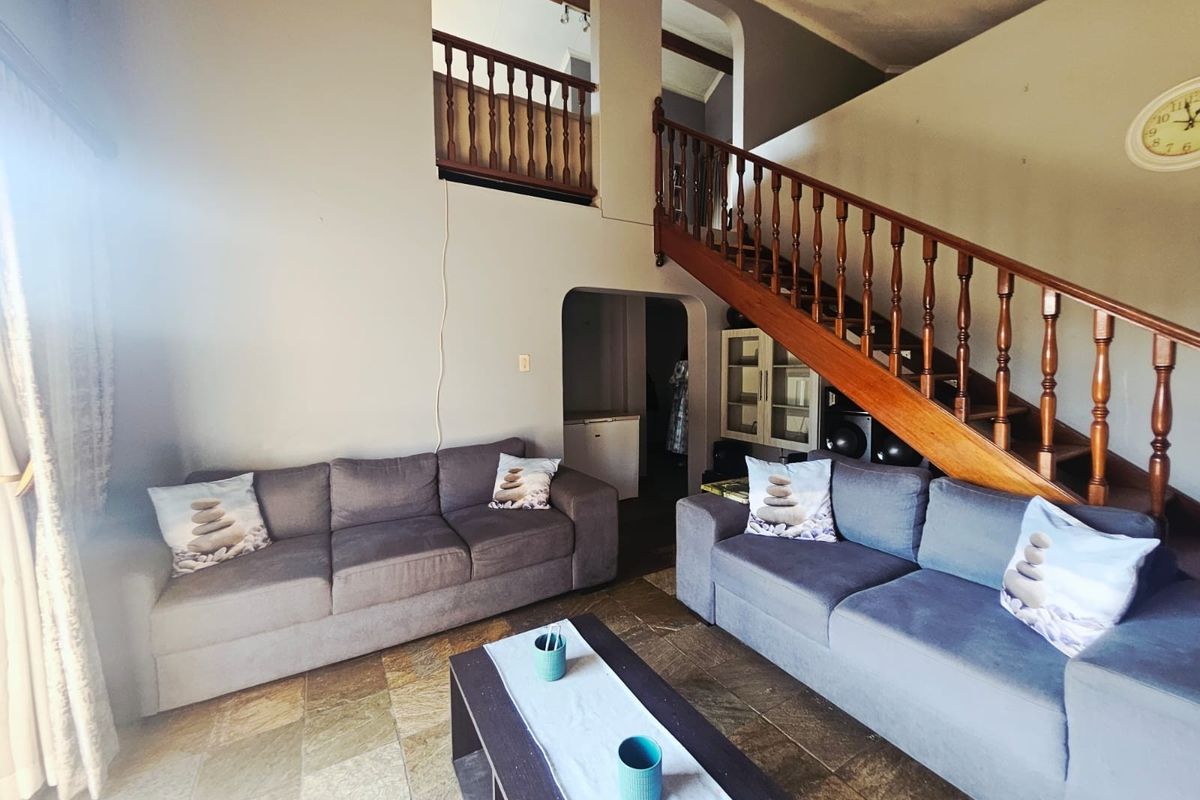 Spacious living room featuring stone tile flooring, a prominent wooden staircase with balustrade, and an open mezzanine level with arched architectural details.