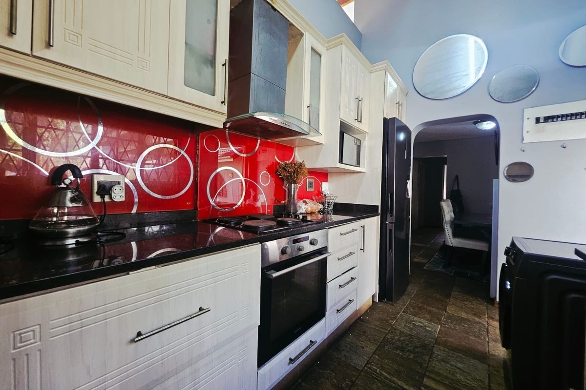 A functional kitchen featuring cream cabinetry, granite countertops, a bold red patterned splashback, and integrated appliances with stone tile flooring.