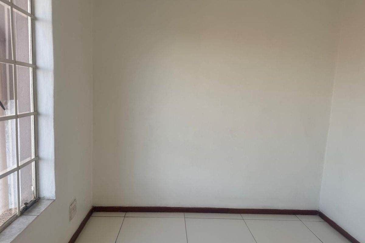 An empty bedroom featuring neutral tiled flooring, white walls, and a window fitted with security burglar bars.