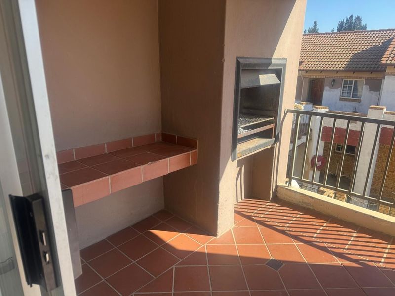A covered balcony featuring a built-in braai, tiled prep counter, and metal railing, offering a functional outdoor entertainment space.