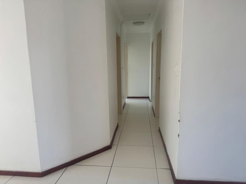 A vacant interior hallway featuring white walls, tiled flooring, and multiple doorways leading to other rooms in the apartment.
