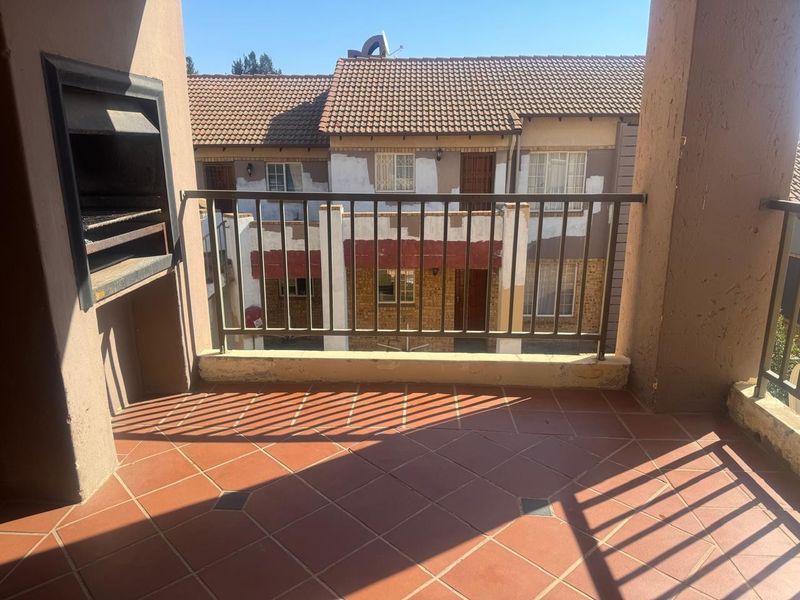 A covered balcony featuring a built-in braai, tiled flooring, and a metal balustrade, overlooking the complex courtyard.