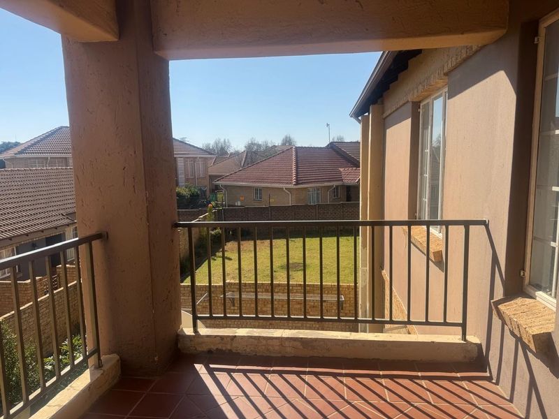 A covered balcony featuring tiled flooring and a metal balustrade, offering an elevated view of the surrounding residential neighborhood and garden area.