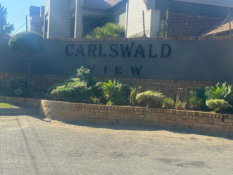 Entrance view of Carlswald View complex featuring a brick boundary wall, paved driveway, and established garden landscaping.