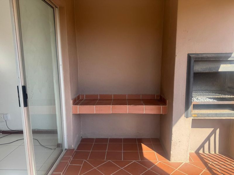 Covered balcony area featuring a built-in braai, tiled prep counter, and terracotta flooring, providing a functional outdoor entertainment space.