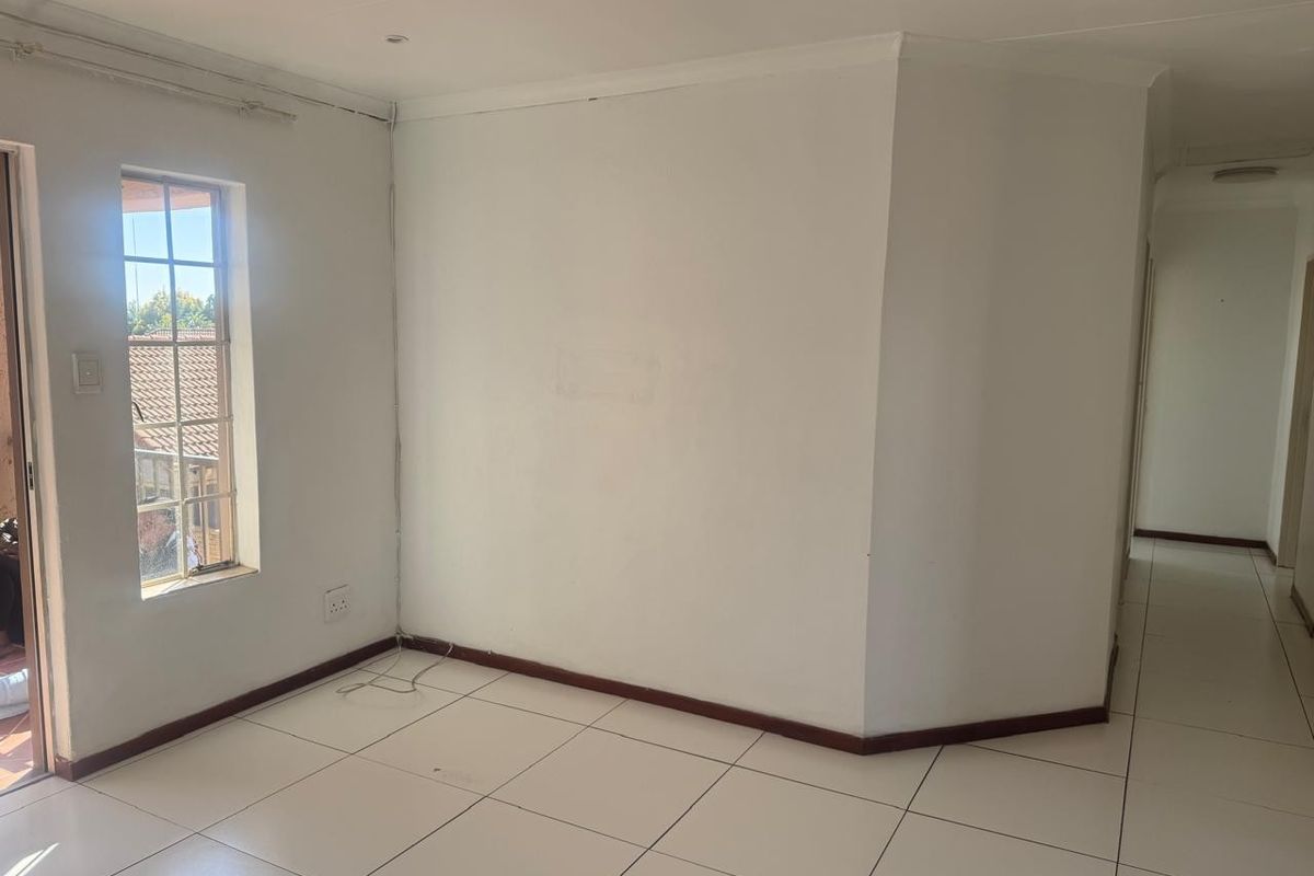 An empty living area featuring white walls, tiled flooring, and a window, providing a blank canvas for interior design.