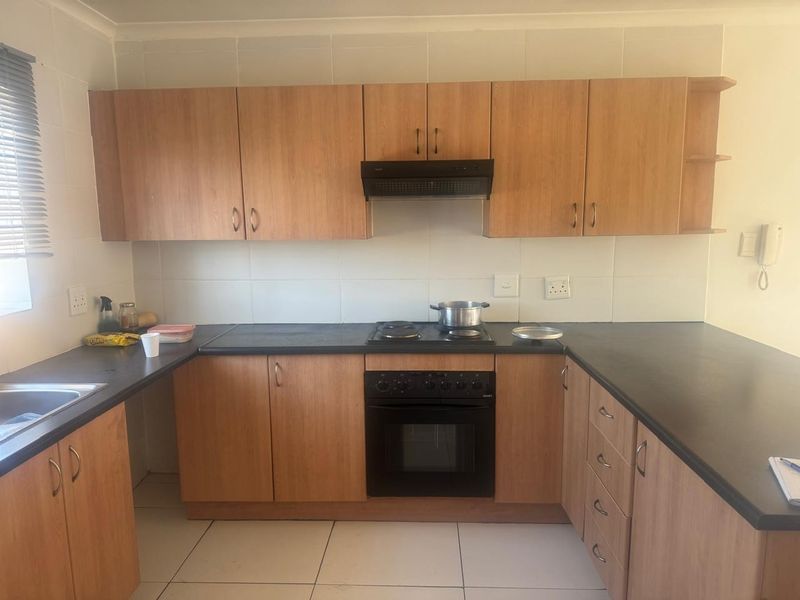 A functional kitchen featuring wood-look cabinetry, dark countertops, built-in oven, electric hob, and tiled splashbacks, offering a clean and practical workspace.