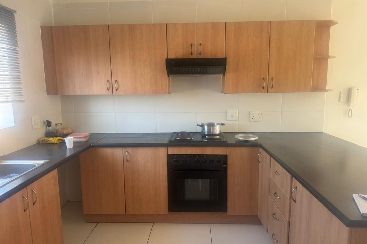 A functional kitchen featuring wood-look cabinetry, dark countertops, built-in oven, electric hob, and tiled splashbacks, offering a clean and practical workspace.