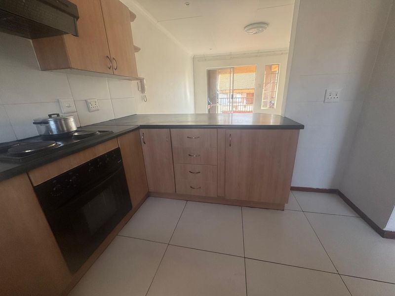 A functional kitchen featuring wood-finish cabinetry, dark countertops, built-in oven and hob, and tiled flooring, with an open-plan layout leading to a balcony.