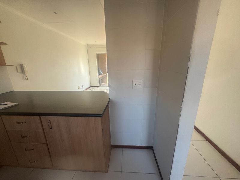 A compact kitchen area featuring built-in wooden cabinetry, dark laminate countertops, and tiled flooring, offering a functional layout ready for updates.