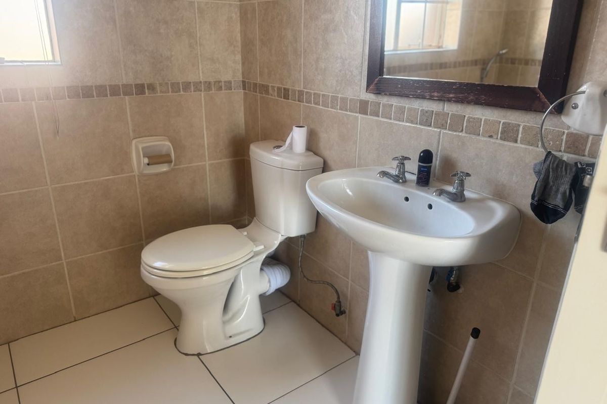 A functional bathroom featuring a pedestal basin, ceramic toilet, and neutral wall and floor tiling.