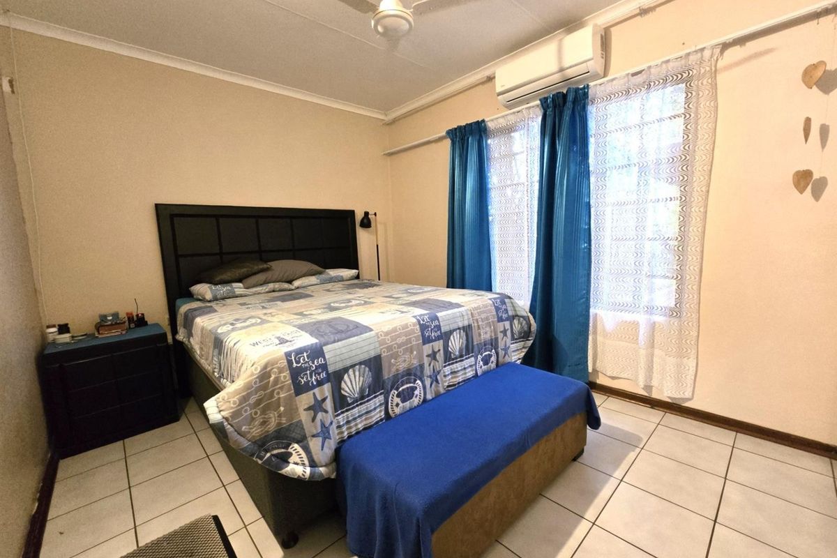 A functional bedroom featuring tiled flooring, a ceiling fan, and a wall-mounted split-system air conditioner for climate control.