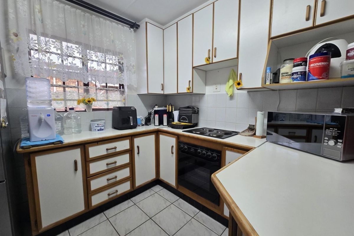 A functional kitchen featuring white laminate cabinetry with wood trim, a built-in oven, electric hob, and tiled flooring.