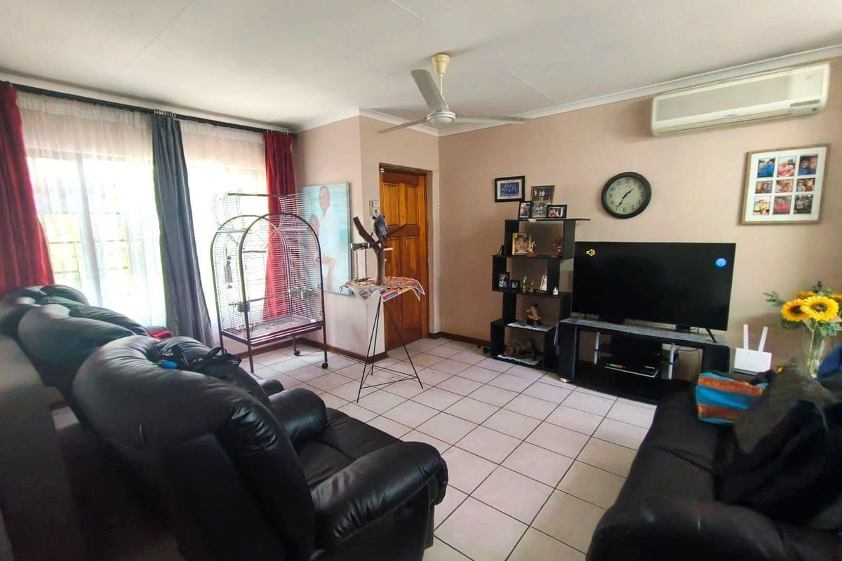A functional living room featuring tiled flooring, a ceiling fan, and a wall-mounted air conditioning unit with access to an outdoor area.