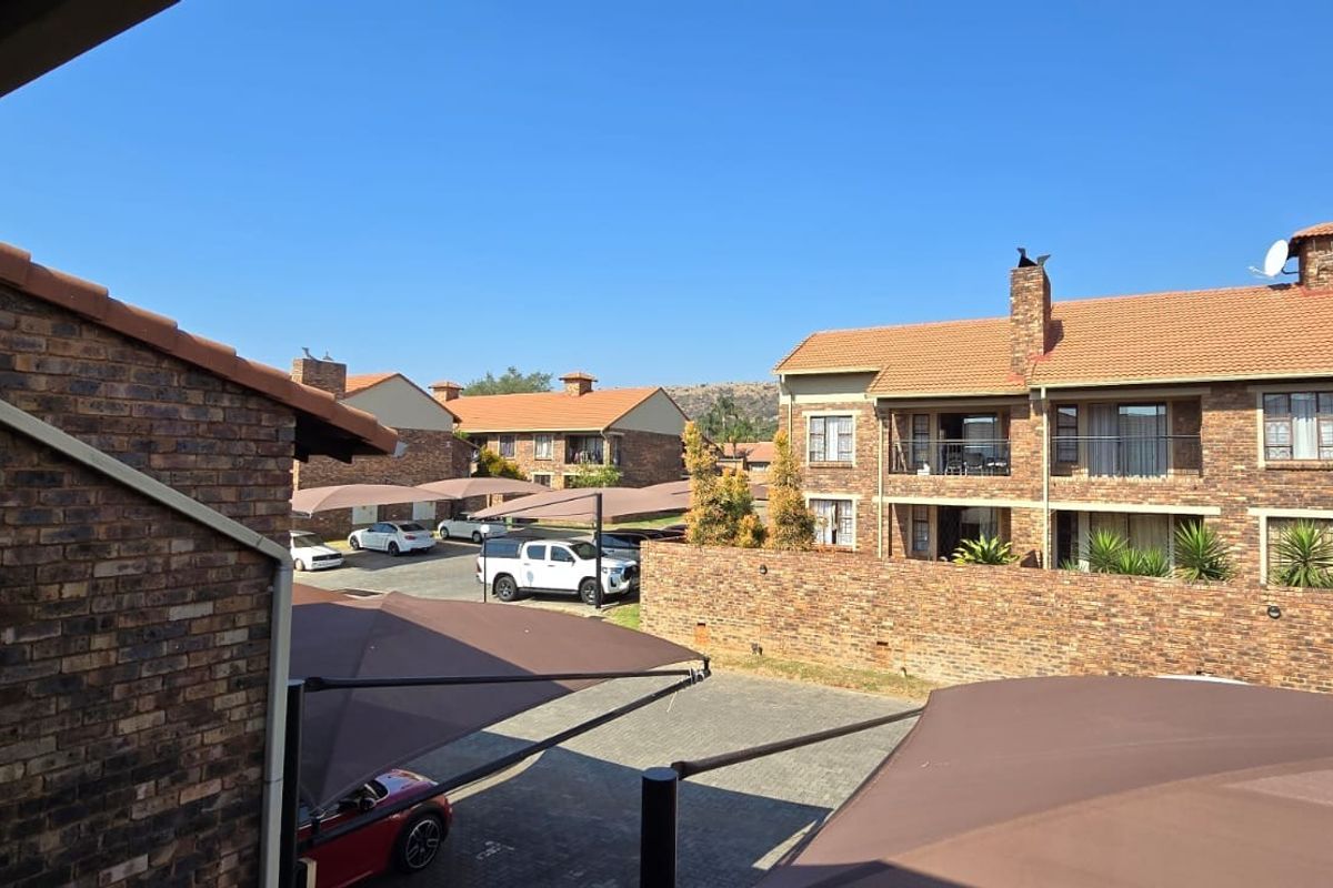 An elevated view of the apartment complex exterior, featuring face brick buildings, tiled roofs, and covered parking bays with shade cloth structures.