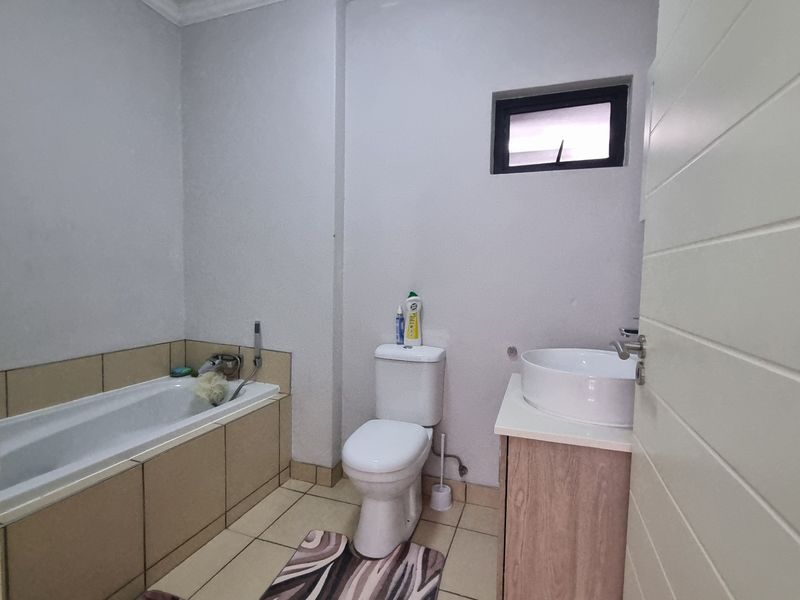 A functional bathroom featuring a built-in bathtub with tiled surround, a modern vessel sink on a vanity cabinet, and a standard toilet.