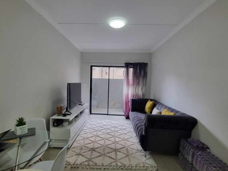 A well-lit living room featuring tiled flooring, cove cornicing, and a sliding glass door providing access to an outdoor area.