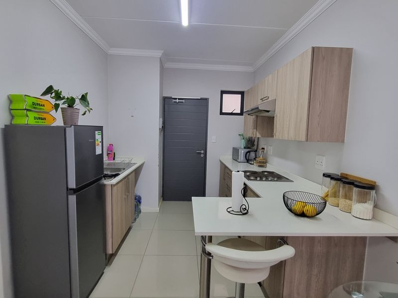Modern kitchen featuring light wood-tone cabinetry, white countertops, integrated hob, extractor fan, and tiled flooring in a clean, functional layout.