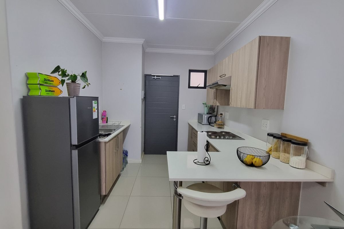 Modern kitchen featuring light wood-tone cabinetry, white countertops, integrated hob, extractor fan, and tiled flooring in a clean, functional layout.