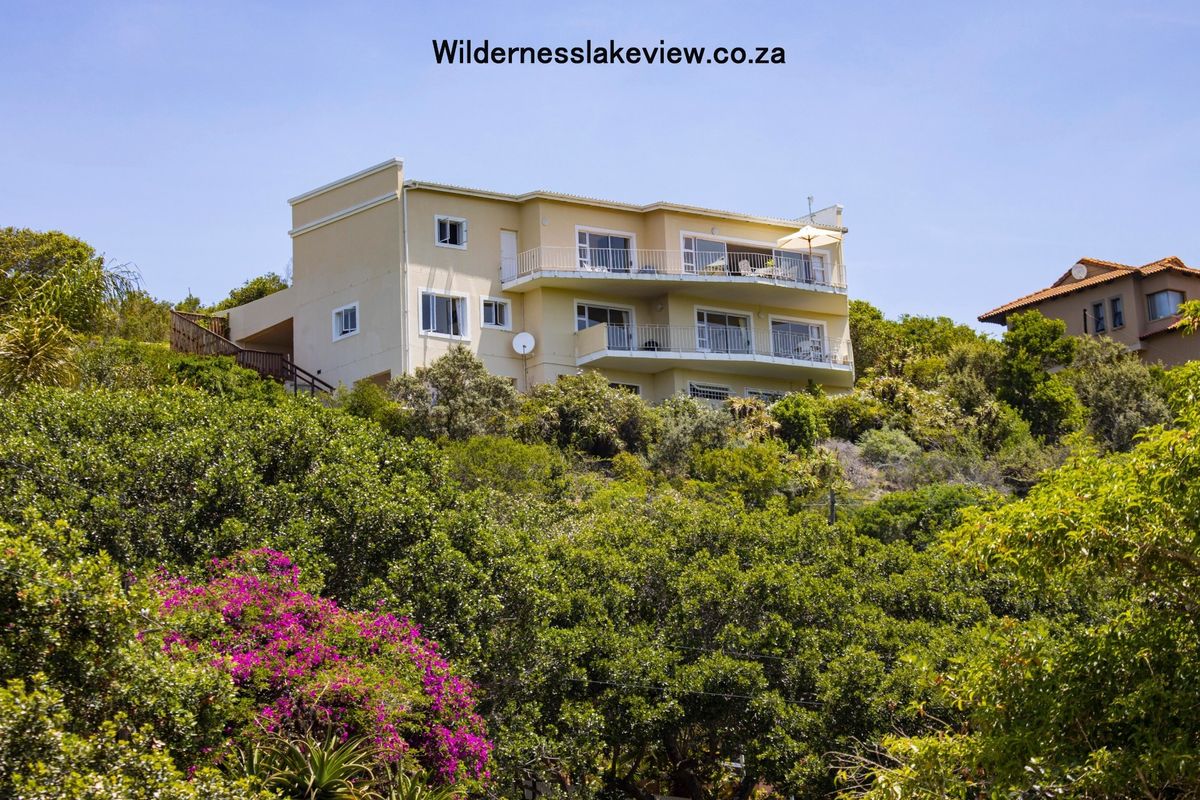 A multi-story residential property featuring tiered balconies and sliding doors, nestled within a lush, elevated garden setting.