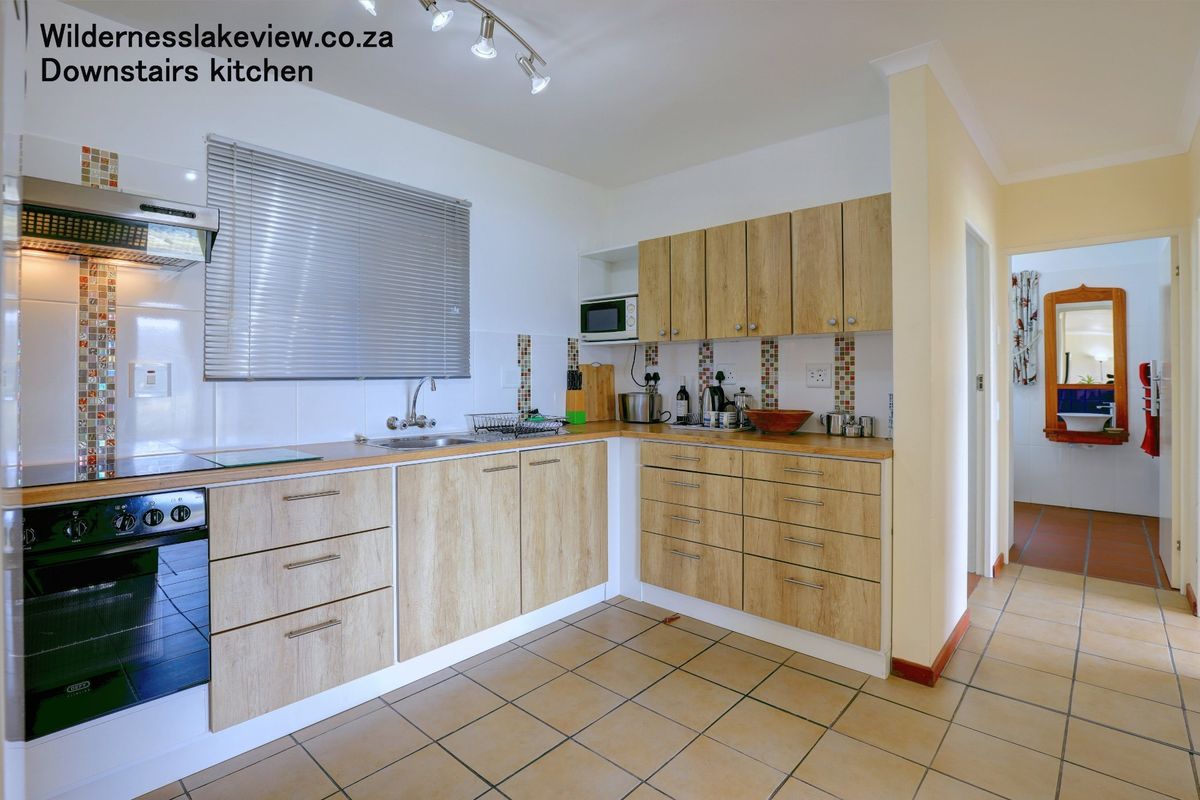 A functional kitchen featuring light wood-finish cabinetry, laminate countertops, built-in oven with extractor fan, and tiled flooring with a decorative backsplash.
