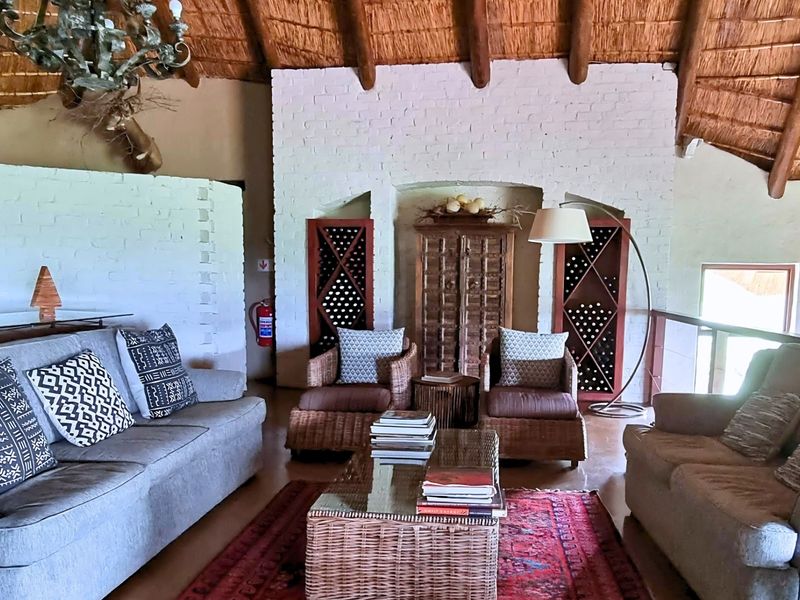 Spacious living area featuring a traditional thatched roof with exposed timber rafters and a distinctive painted brick feature wall with integrated wine storage.