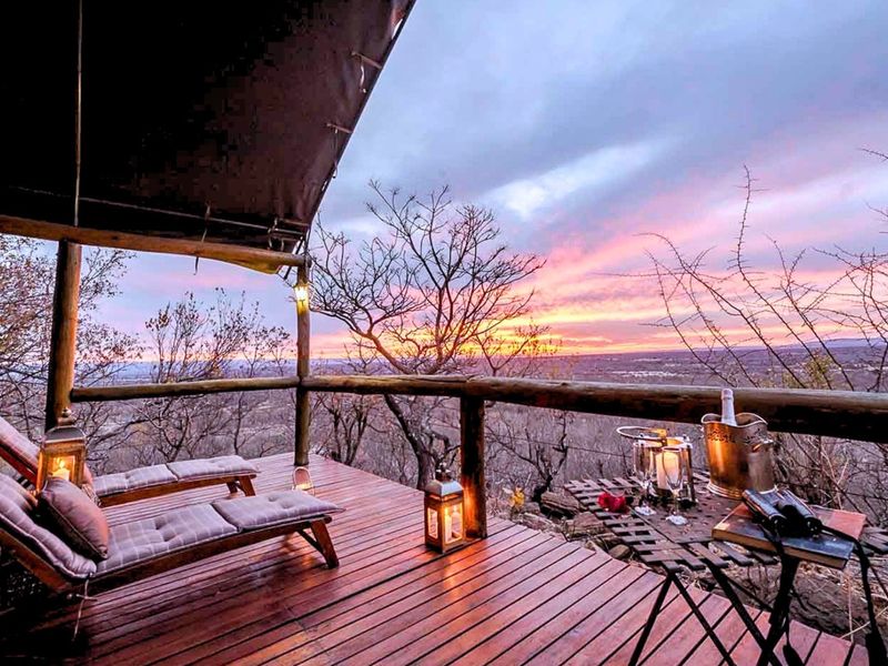 Elevated timber deck with a canvas roof, offering expansive panoramic views of the surrounding landscape at sunset.