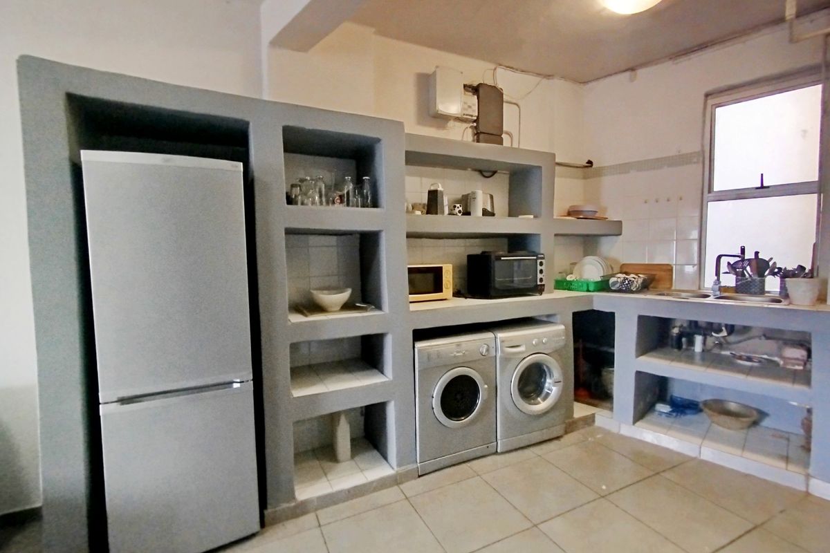 A functional kitchen featuring built-in concrete shelving, tiled flooring, and integrated laundry appliance spaces, offering a practical layout with potential for modern updates.