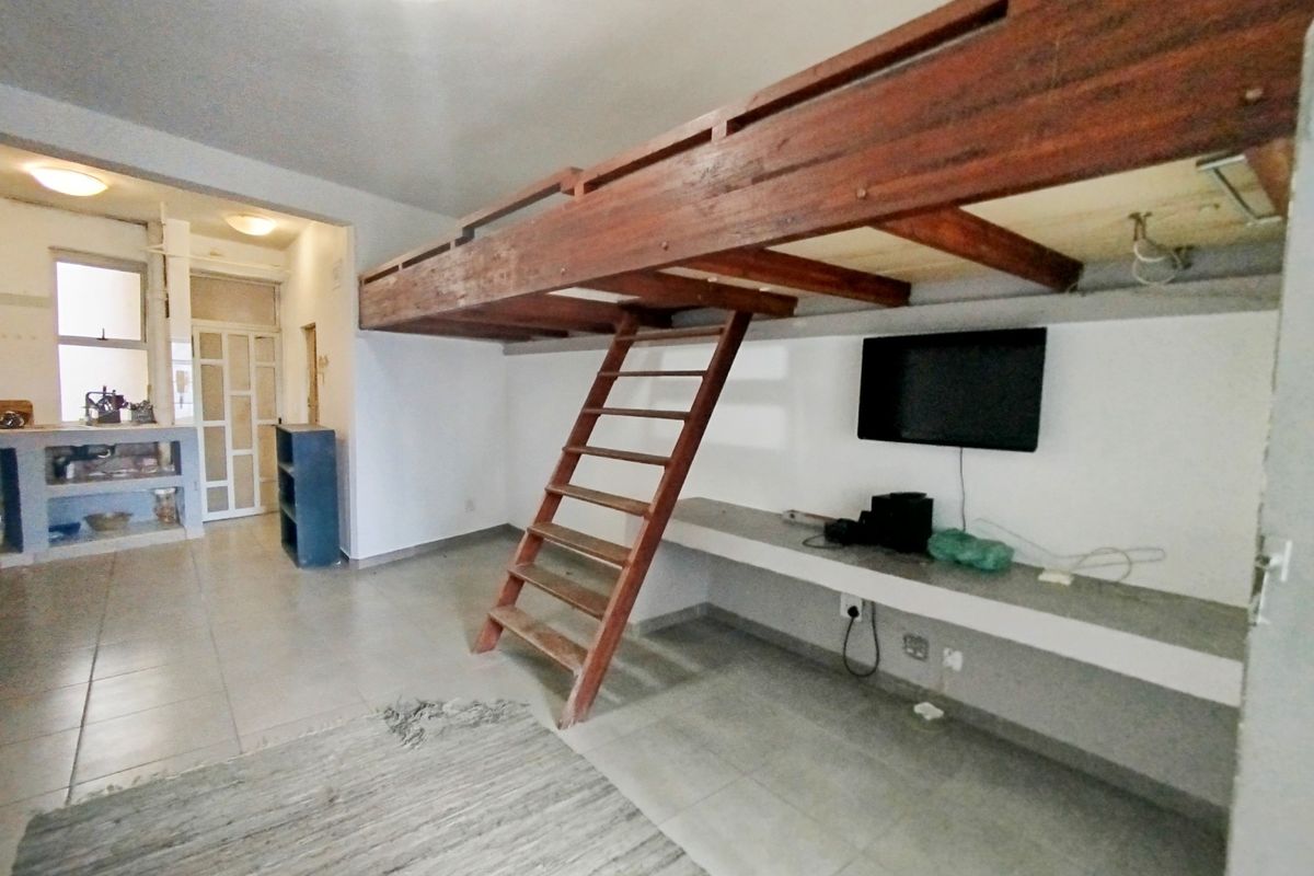 Bedroom featuring a built-in loft bed structure with a wooden ladder and a fixed concrete desk, offering a unique space-saving layout.