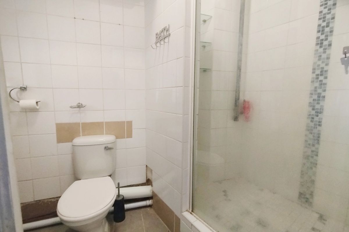 A dated bathroom featuring a toilet and a shower enclosure with visible wear, missing tiles, and exposed plumbing, requiring renovation.