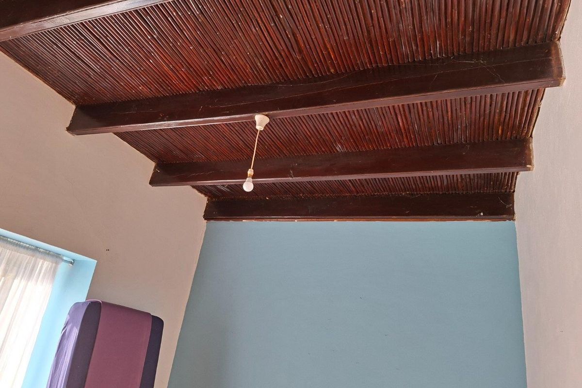 A bedroom interior featuring a rustic reed ceiling with exposed timber beams and a simple pendant light fixture.