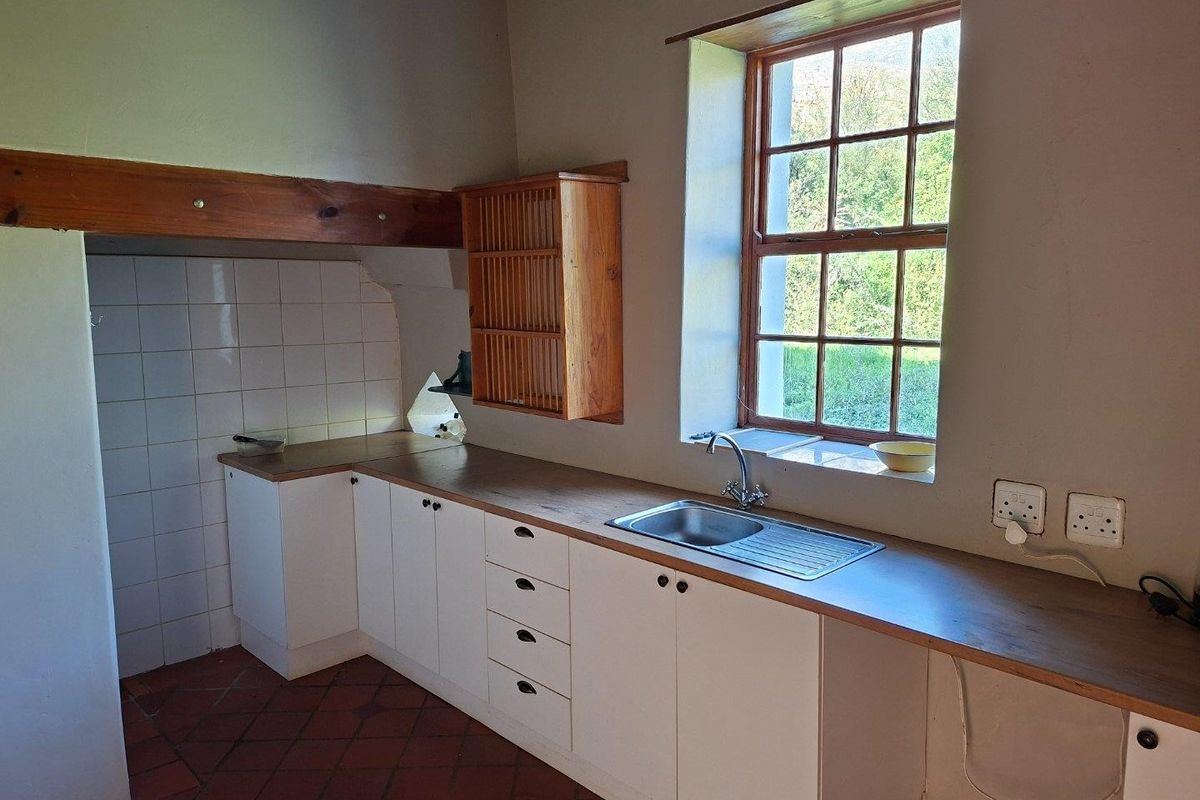 A rustic kitchen featuring white cabinetry, wooden countertops, a stainless steel sink, and traditional terracotta flooring with an exposed timber beam.