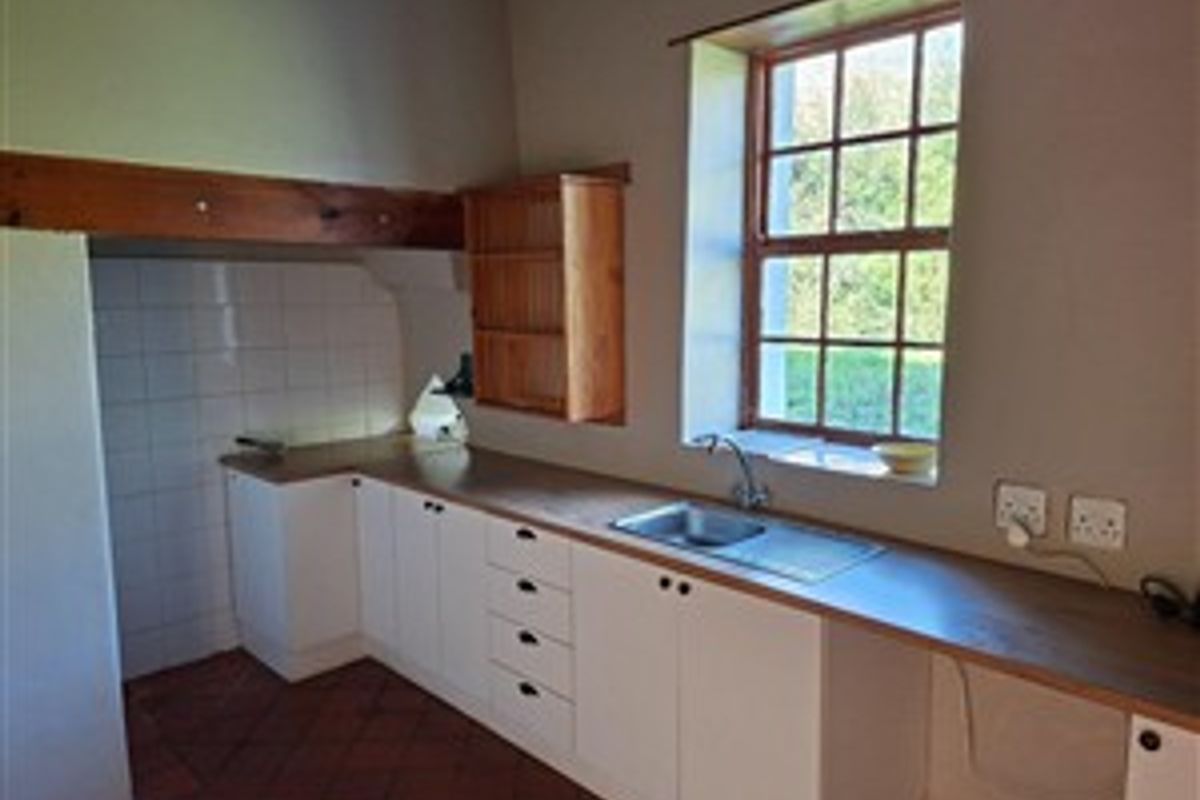 A functional kitchen area featuring white cabinetry, a stainless steel sink, terracotta flooring, and a rustic timber beam, offering a classic farmhouse aesthetic.