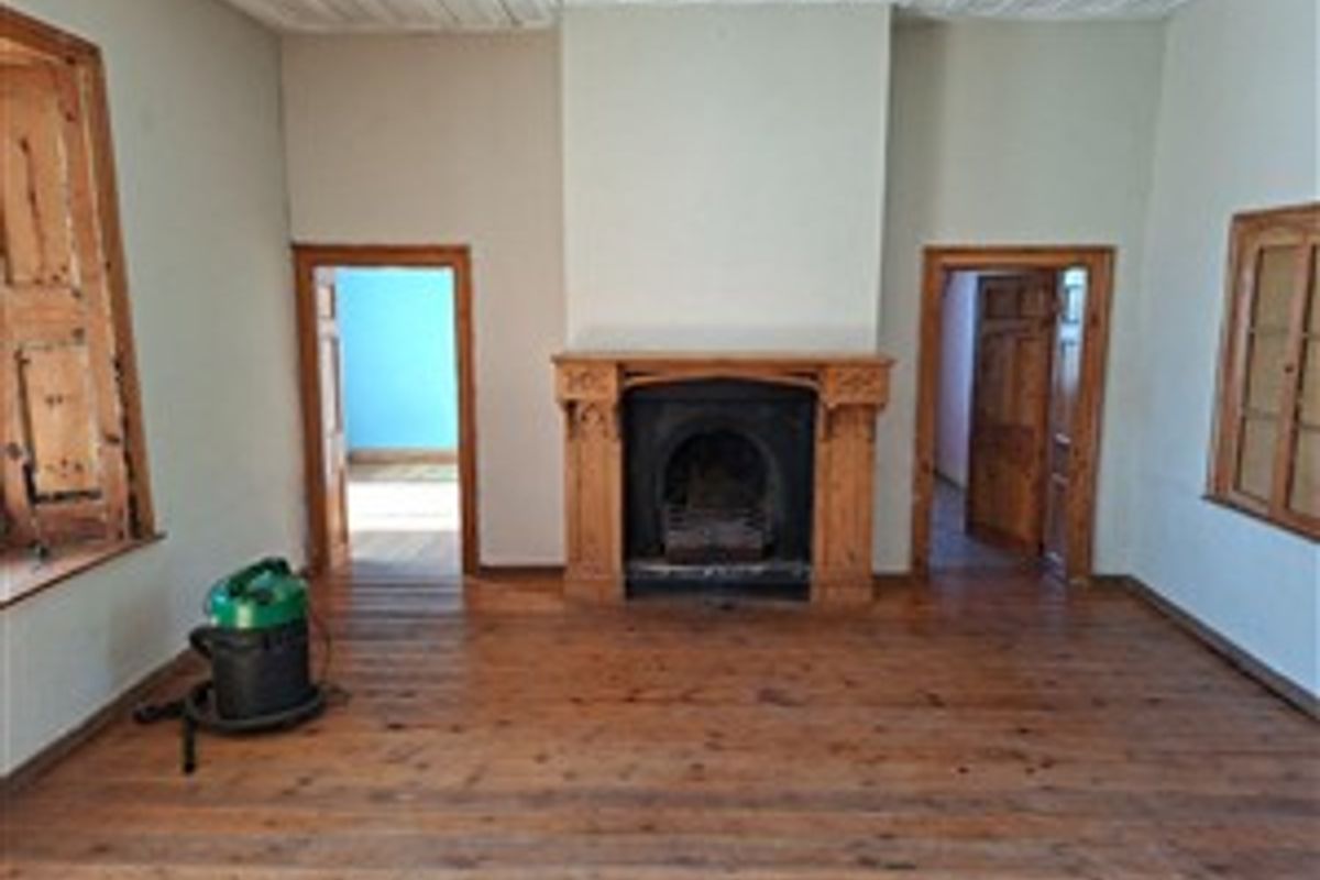 Spacious living room featuring original timber flooring, a classic cast iron fireplace with a wooden mantel, and traditional timber window shutters.