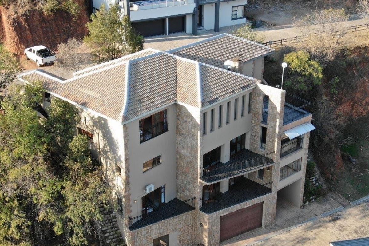 Aerial view of a multi-story residential property featuring stone cladding, tiled roofing, and multiple balconies set against a hillside.