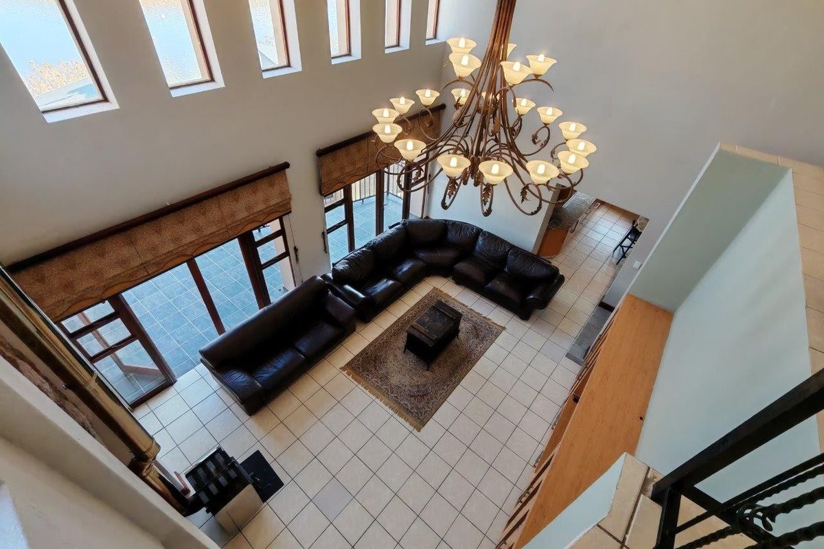 Spacious double-volume living room featuring large windows, tiled flooring, and a prominent wrought iron chandelier, offering access to an outdoor patio area.