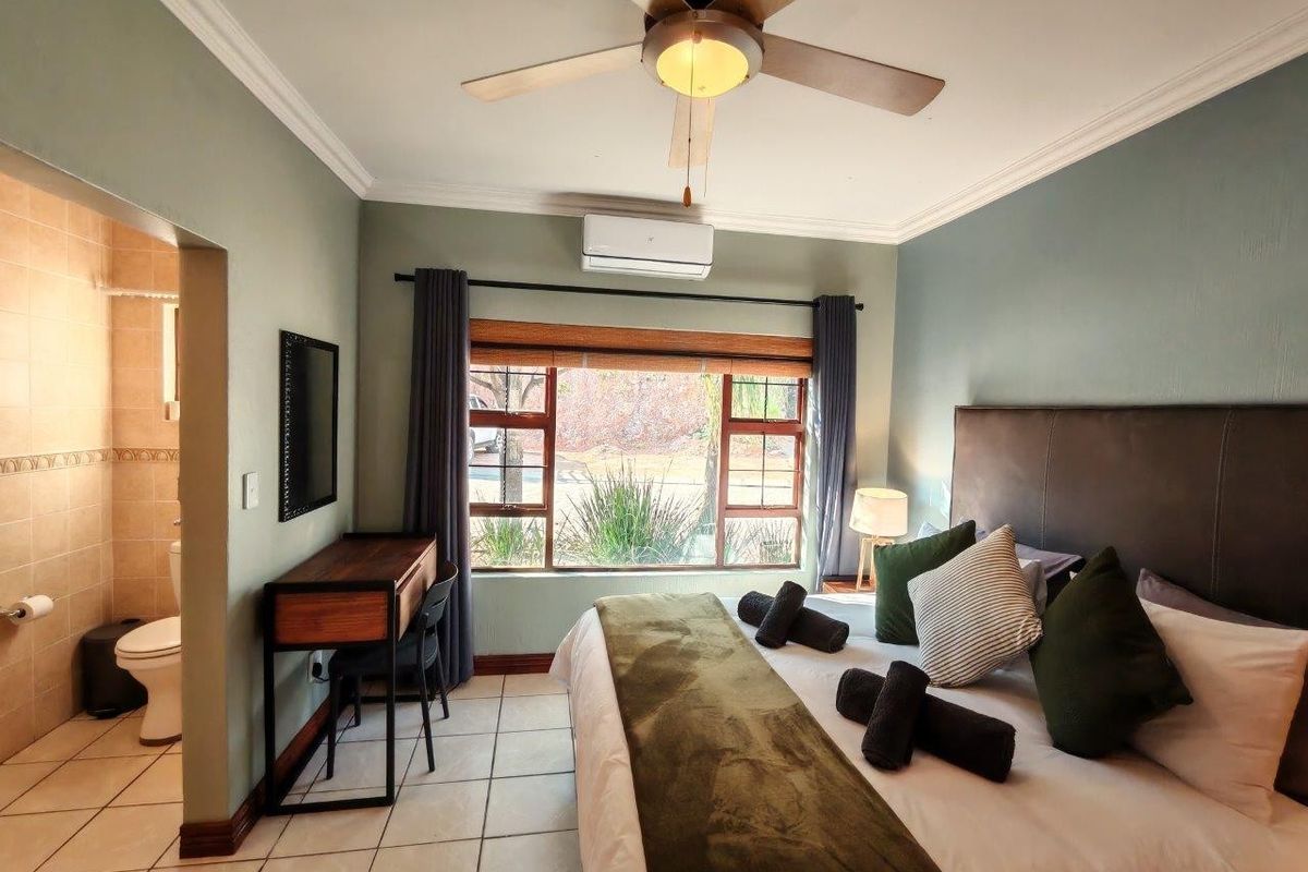 A well-maintained bedroom featuring tiled flooring, a ceiling fan, split-system air conditioning, and an adjoining en-suite bathroom.