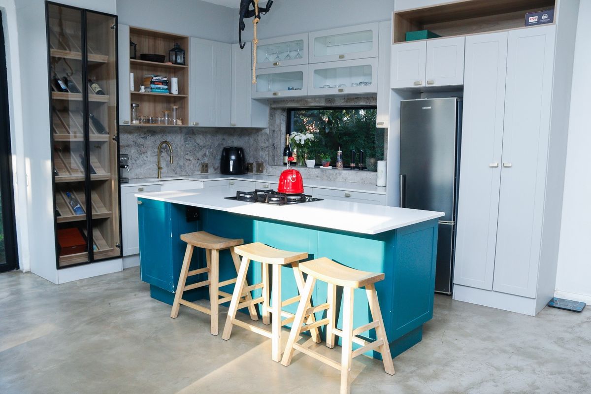 Modern kitchen featuring a vibrant teal island with gas cooktop, stone countertops, custom cabinetry, integrated wine storage, and polished concrete floors.