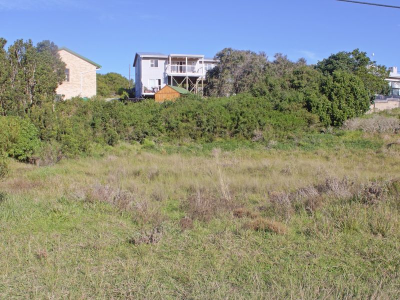 A view of a vacant residential plot featuring natural vegetation and surrounding established residential properties.