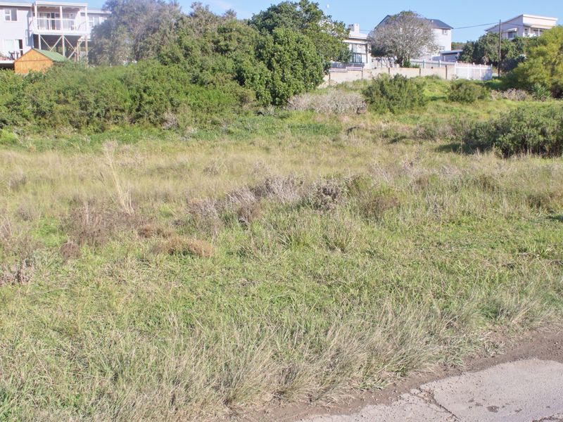 A view of a vacant residential plot featuring natural grassland and a gentle slope, situated in a developed neighborhood.