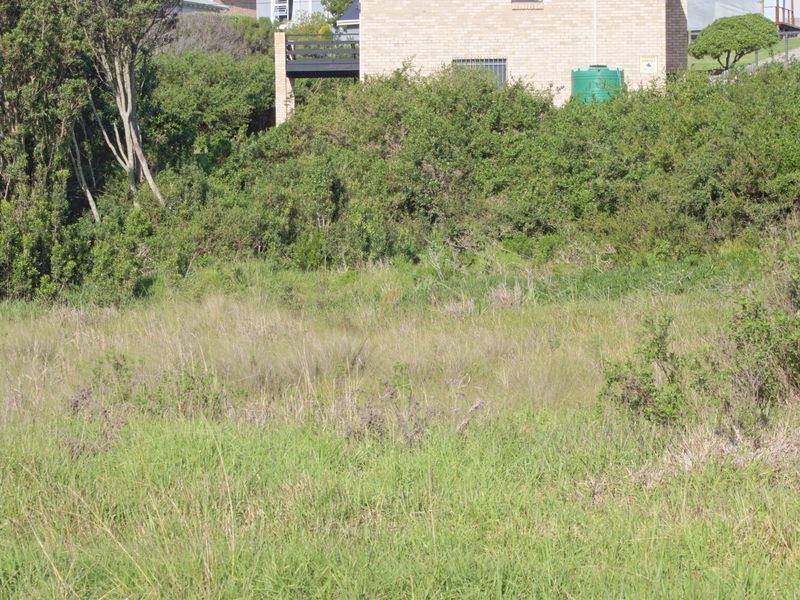 A view of a vacant residential plot featuring natural vegetation and a water tank, with neighboring property visible in the background.