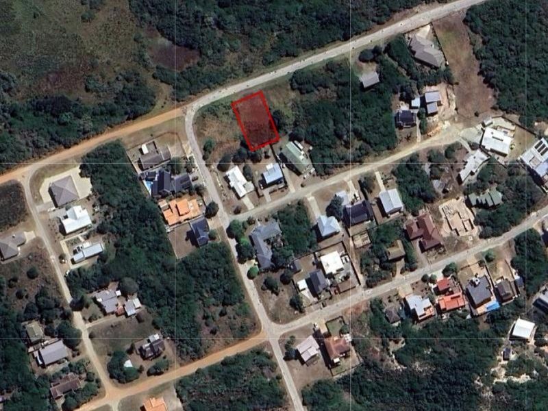 Aerial view of a vacant residential land plot highlighted in red, situated within an established neighborhood with surrounding vegetation and road access.