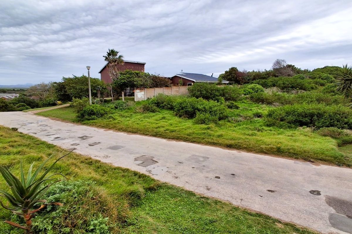 A street view showing the paved access road, boundary wall, and surrounding natural vegetation of the residential vacant land plot.