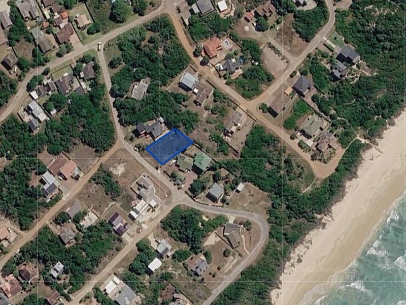 An aerial view of a vacant residential plot located in a coastal neighborhood, highlighting its position relative to the beach and surrounding properties.