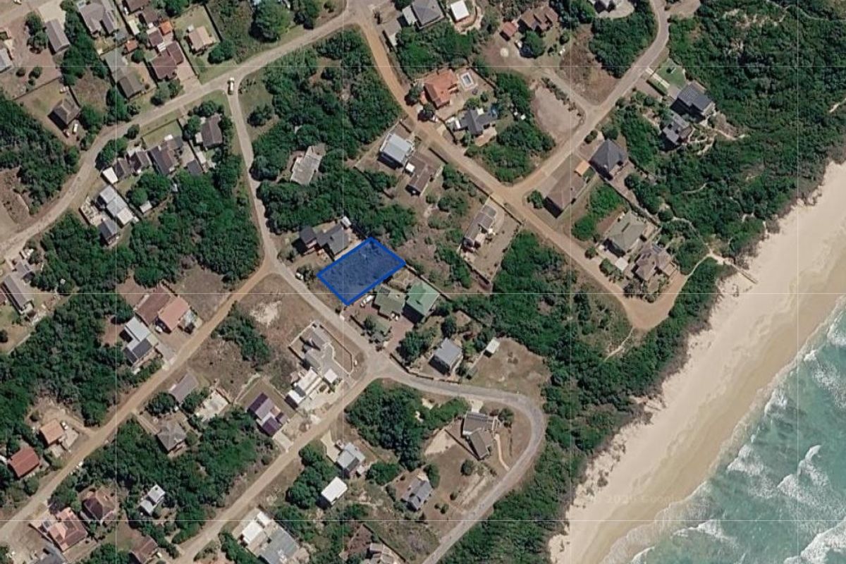 An aerial view of a vacant residential plot located in a coastal neighborhood, highlighting its position relative to the beach and surrounding properties.