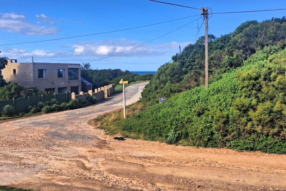A view of the unpaved access road leading towards the coast, featuring surrounding vegetation, utility infrastructure, and nearby residential boundary walls.