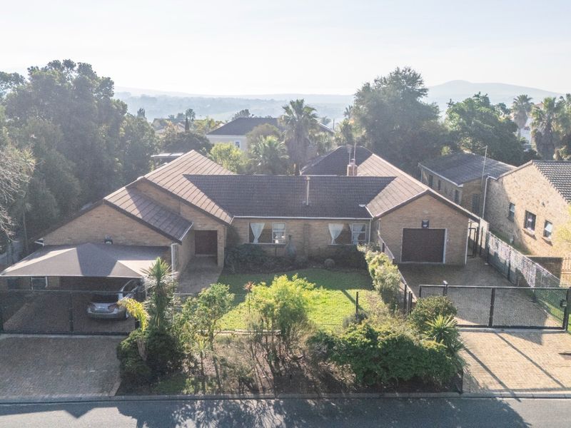 Aerial view of a single-story brick house featuring a tiled roof, paved driveway, carport, garage, and a well-maintained front garden.