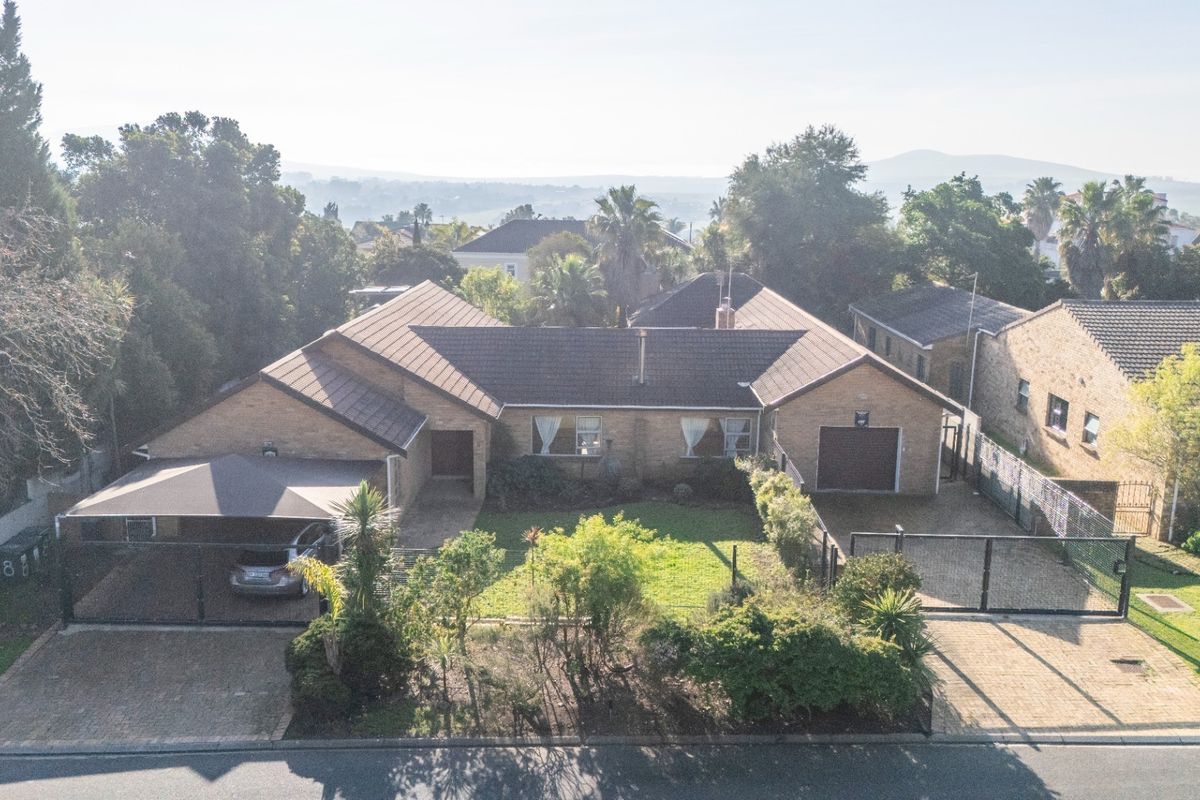 Aerial view of a single-story brick house featuring a tiled roof, paved driveway, carport, garage, and a well-maintained front garden.